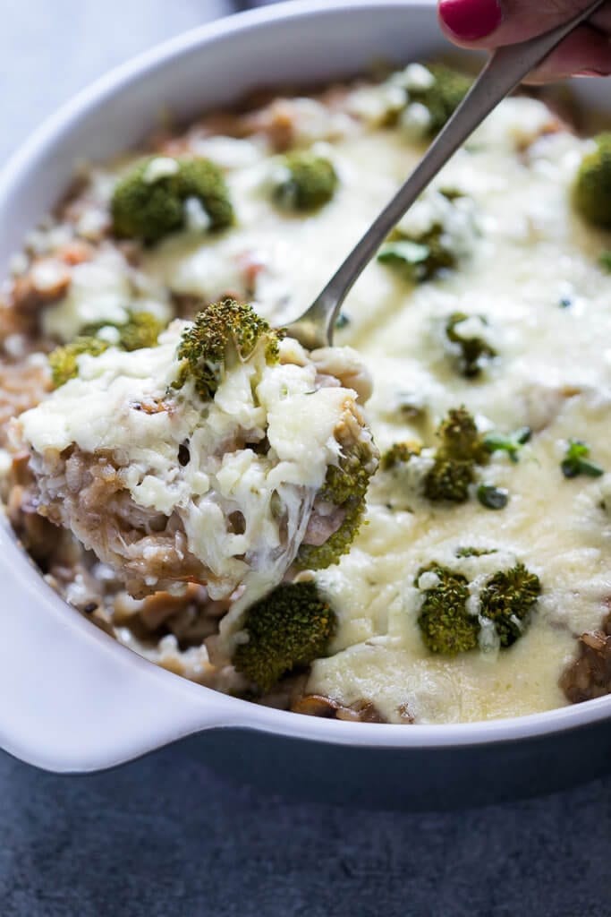 Broccoli chicken and rice casserole in white dish being scooped out with spoon.