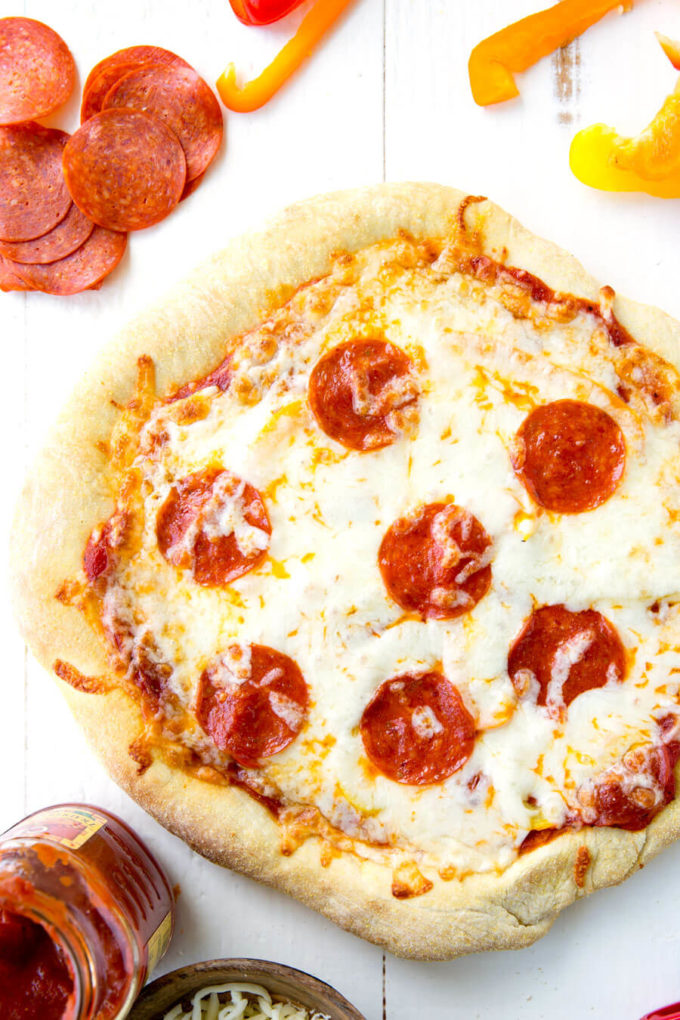 Cheese and pepperoni pizza, surrounded by various pizza toppings. 