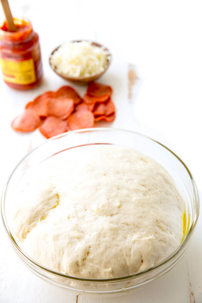 Rising homemade pizza dough in a glass mixing bowl. 