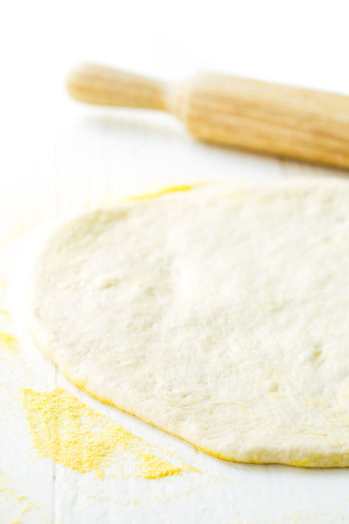 Rolled out homemade pizza dough, lying next to a rolling pin.