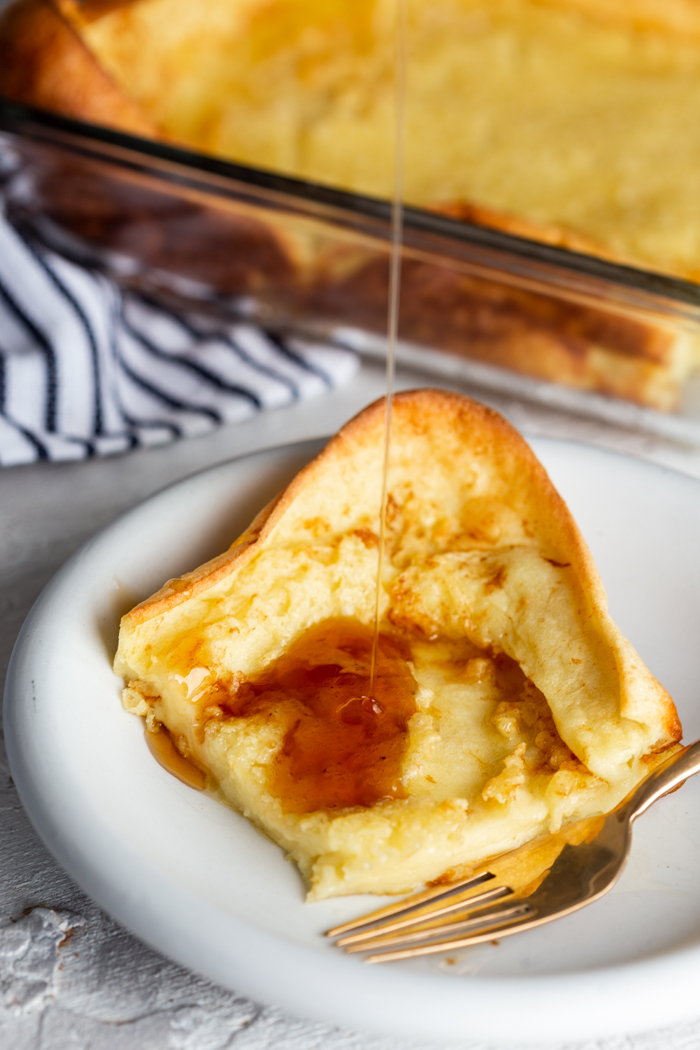 German pancakes, on a white plate with syrup being poured on top