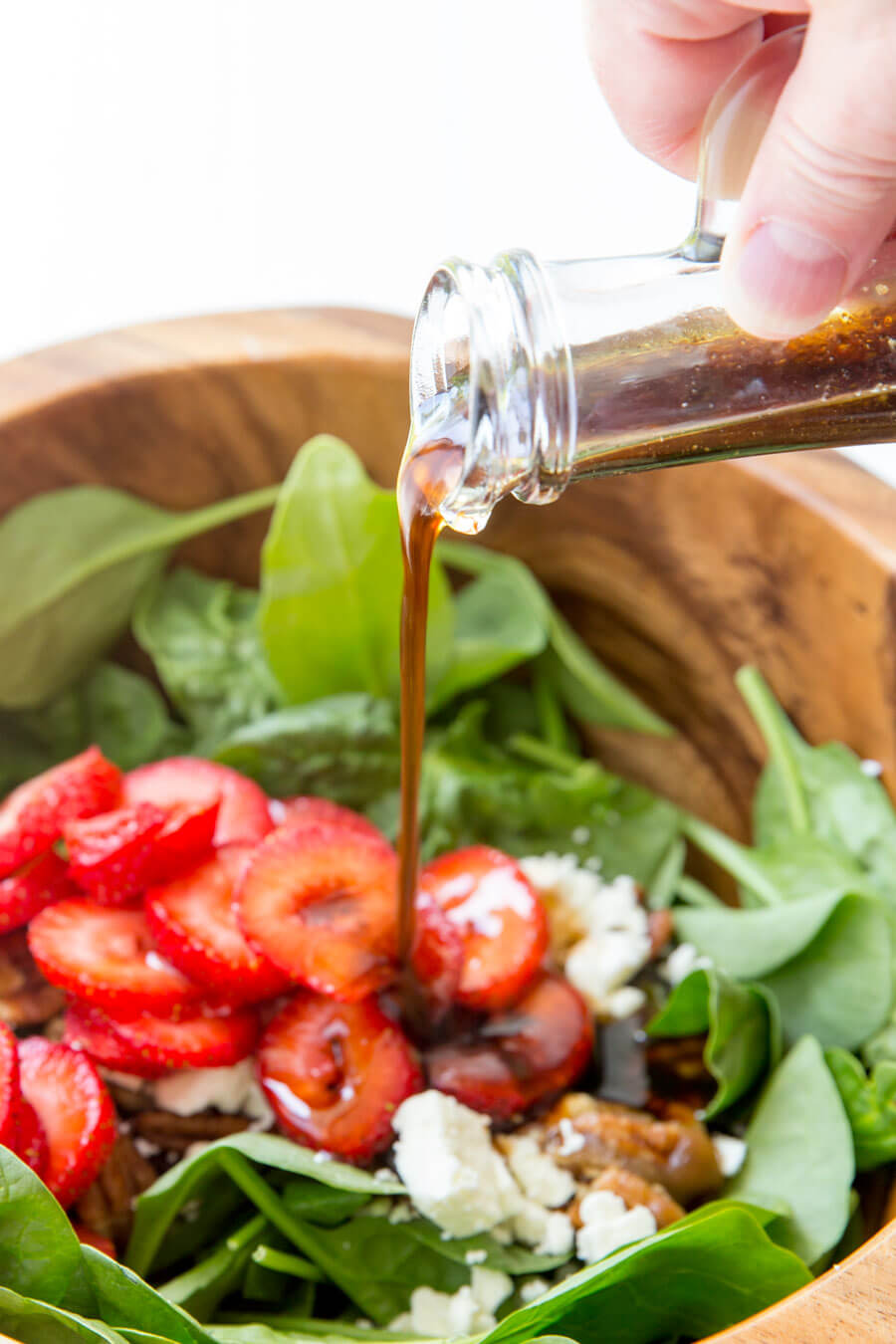 Strawberry Pecan Spinach Salad in wooden bowl with dressing being poured on.