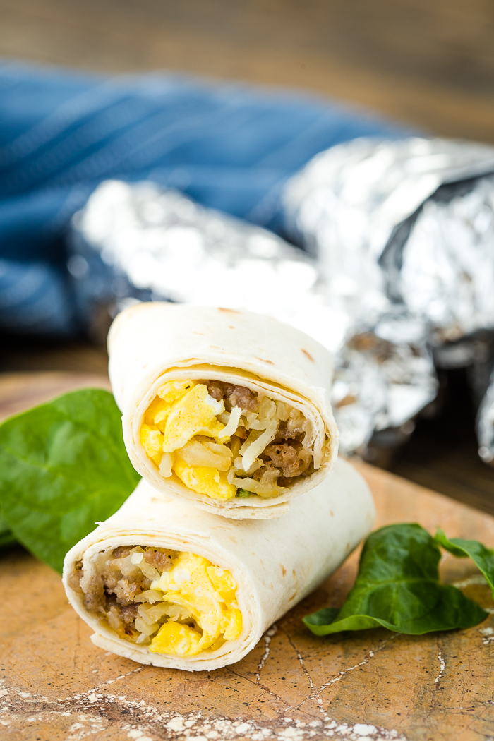 A cut breakfast burrito, stacked on top of each other, foil wrapped burrito in the background. 