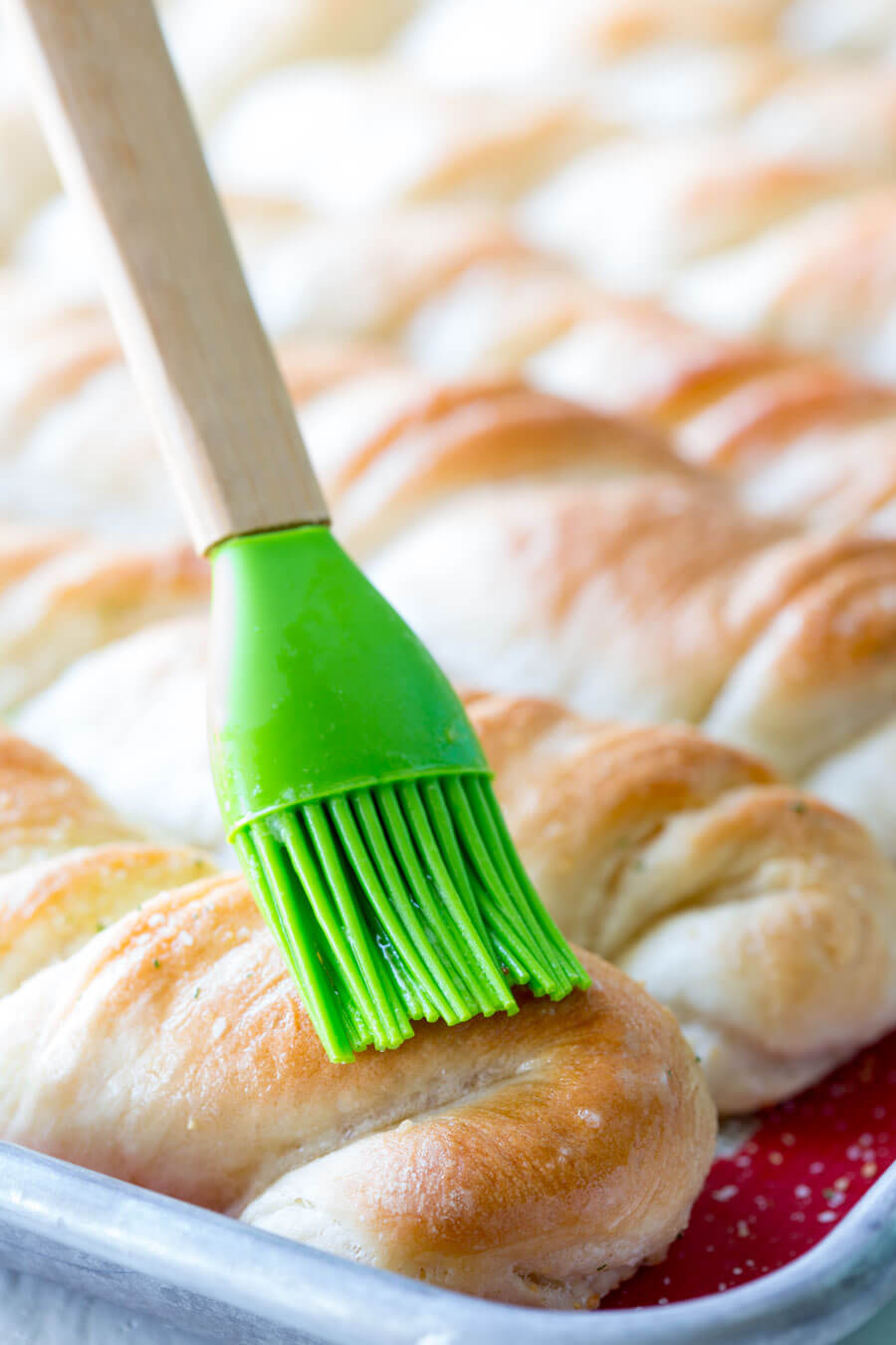 pastry brush spreading garlic butter on top of freshly baked garlic bread twists