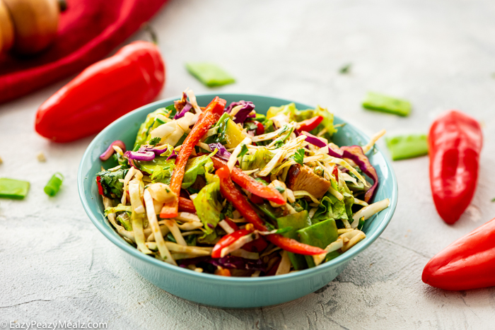 a salad in a blue bowl with red peppers on the side under a counter top