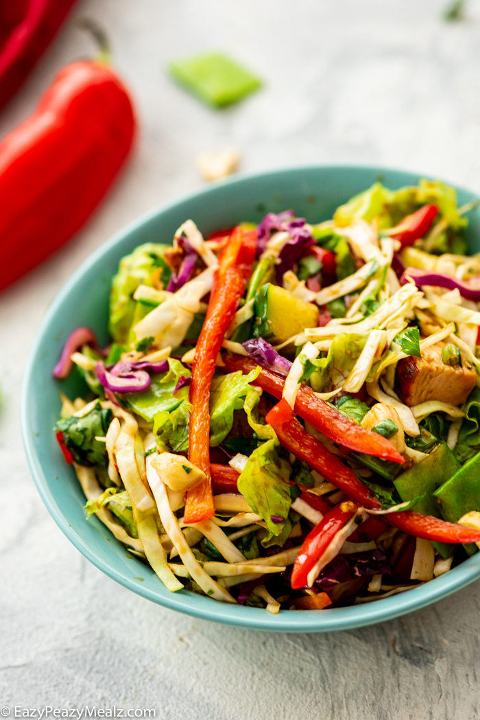 a salad in a blue bowl with a red pepper on the side.