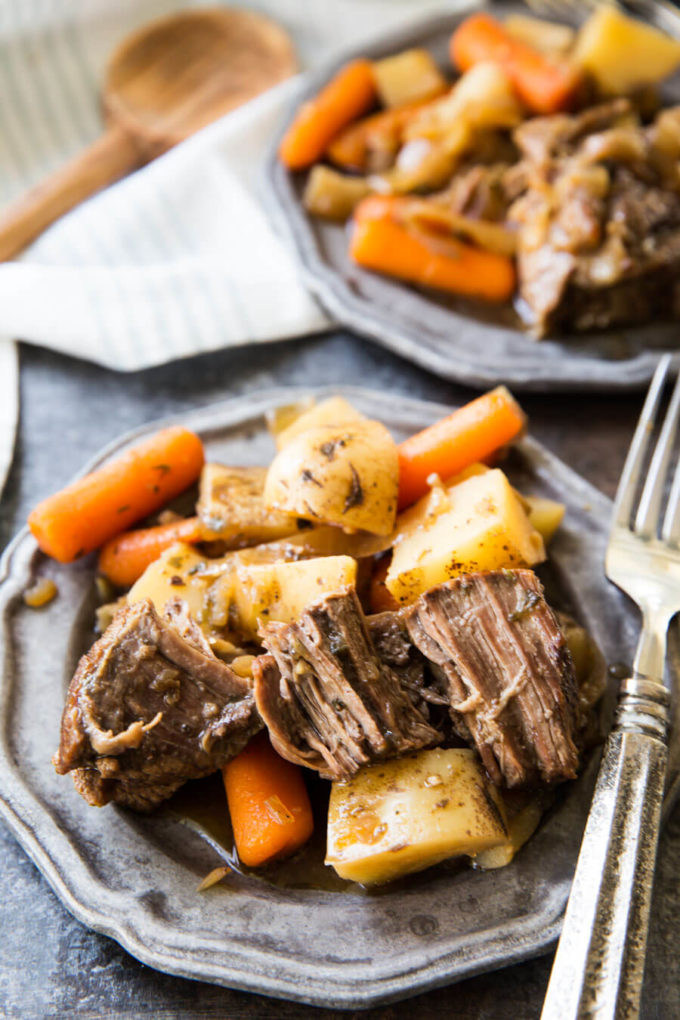 Crock pot chuck roast with potatoes and carrots 2 silver plates with a fork over one plate