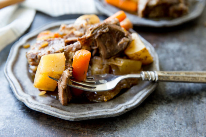 Delicious pot roast with potatoes and carrots on a silver plate with a fork with a piece of roast, potato, and a carrot stuck on it