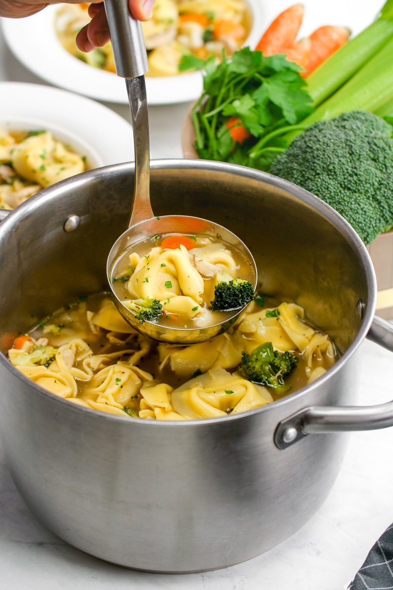 Chicken tortellini soup in a soup pot with a ladel