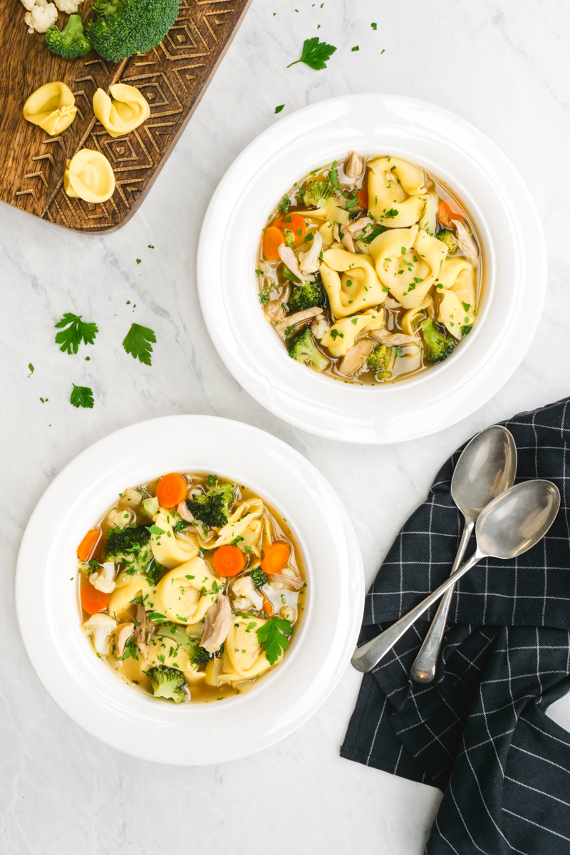 two bowls filled with chicken tortellini soup and vegetables