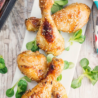 A top down shot of a platter of baked sesame drumsticks with green garnish