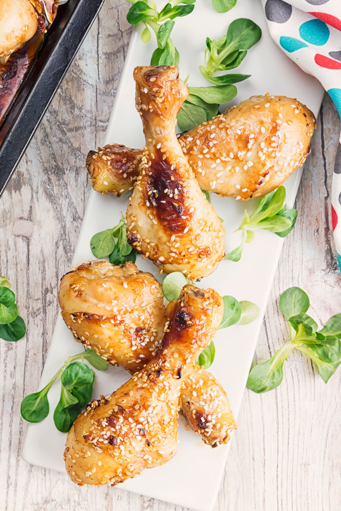 A top down shot of a platter of baked sesame drumsticks with green garnish