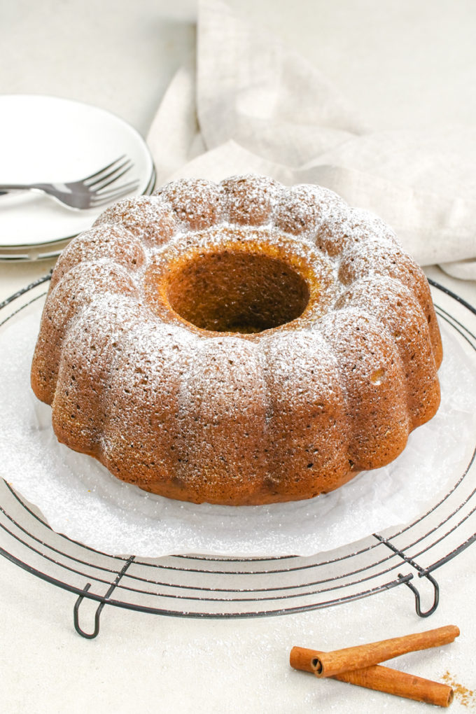 A rich and moist pumpkin bundt cake recipe, with a pumpkin bundt dusted in powdered sugar and sitting on a cooling rack
