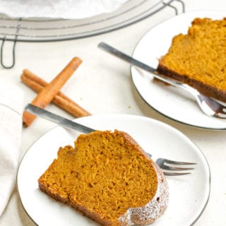 Two white plates each holding a piece of pumpkin cake, a few sticks of cinnamon, and forks