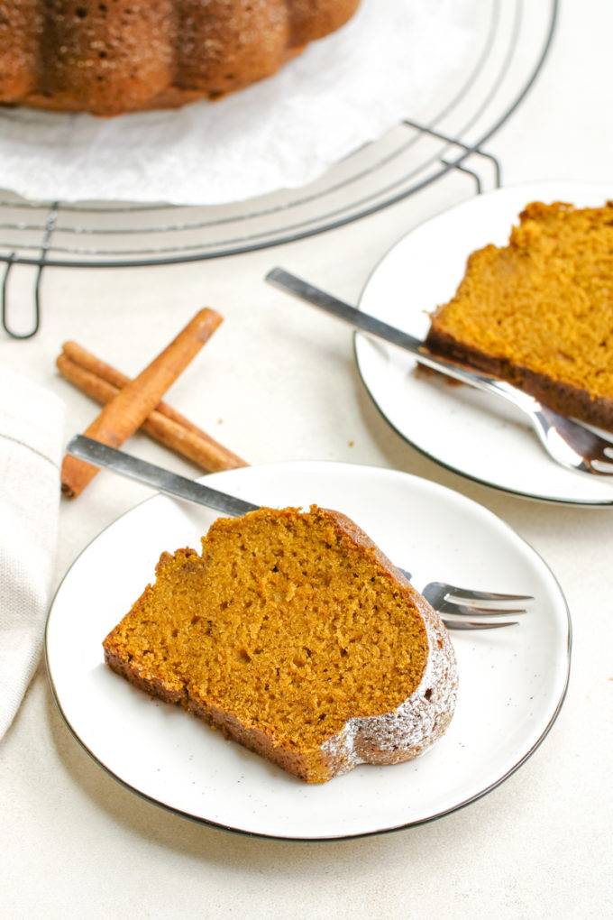 Two white plates each holding a piece of pumpkin cake, a few sticks of cinnamon, and forks