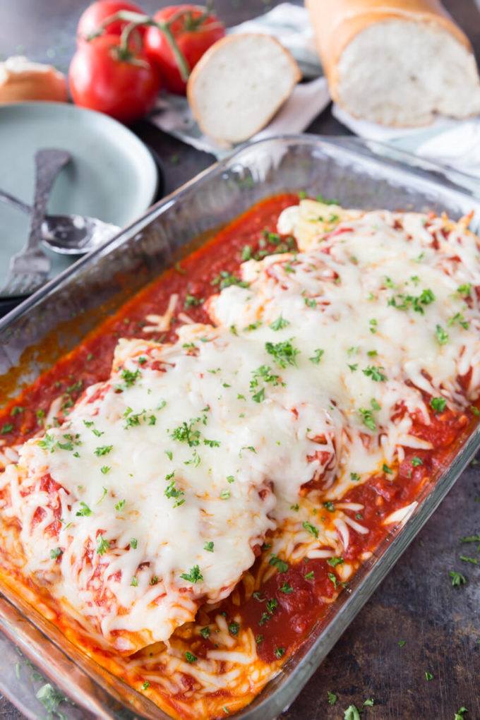a dish of freshly baked stuffed chicken and cheese manicotti covered with pasta sauce and cheese with herbs for garnish