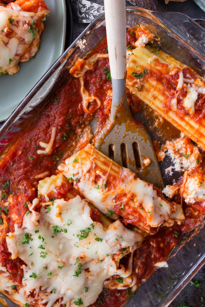 Cheese topped stuffed manicotti in a glass baking dish with a spatula