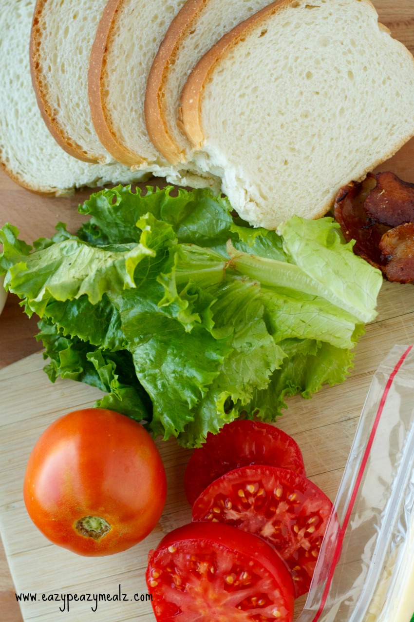sandwich elements such as bread, lettuce, tomatoes and bacon under a wooden platter