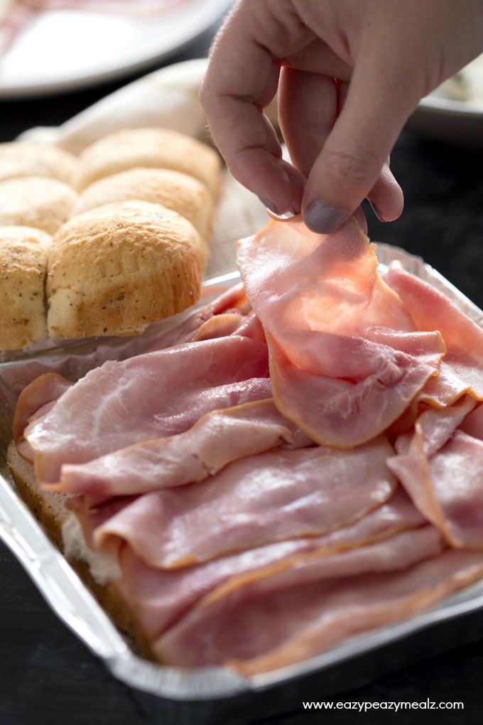 Cheesy Ham and Garlic Sandwich Bake: sliced rolls being filled with cream cheese and sliced ham by a woman