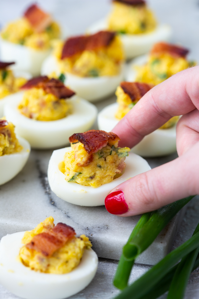 a hand grabbing a bacon cheddar ranch deviled egg off a tray of deviled eggs
