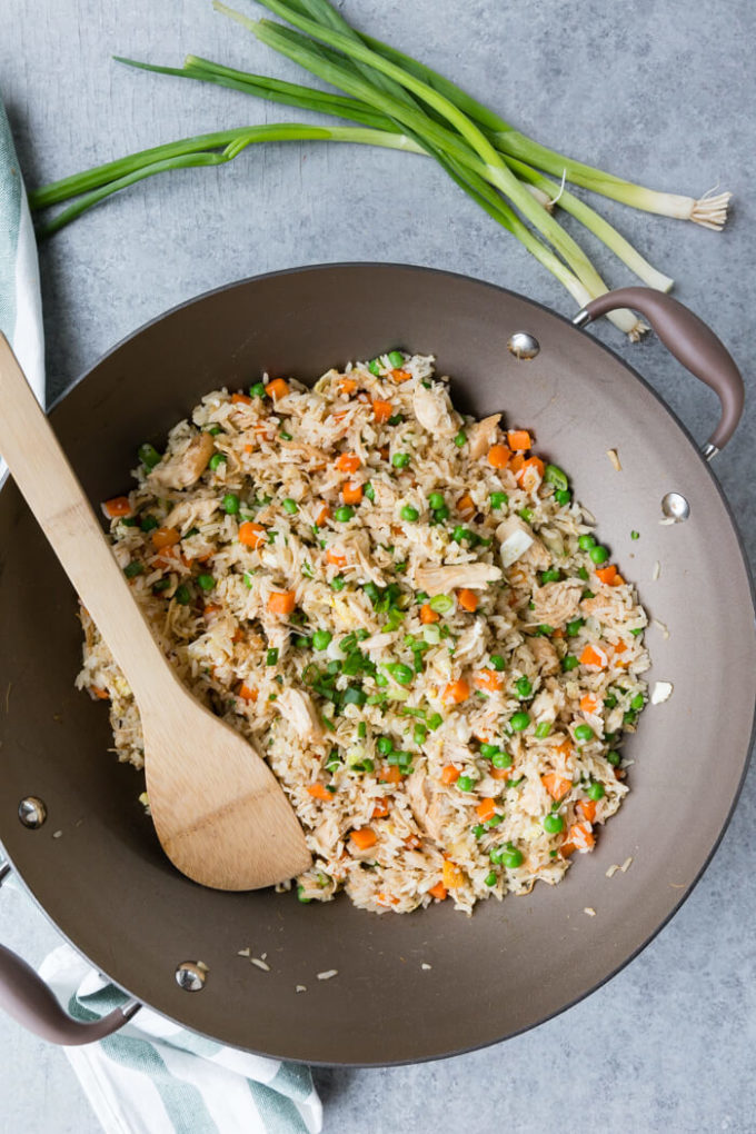 chicken fried rice in a pan with a wooden spoon and green onions.