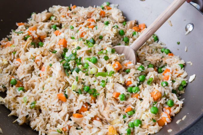 chicken fried rice in a pan with a wooden spoon.