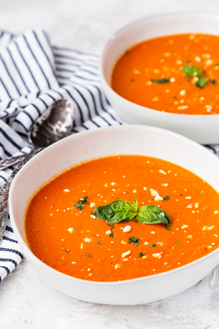 two white bowls of tomato soup with feta cheese and basil 