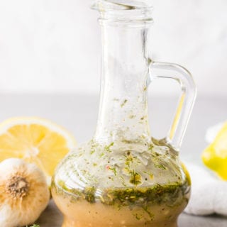 Bottle of Greek Chicken Marinade with lemons, garlic, and herbs around it.