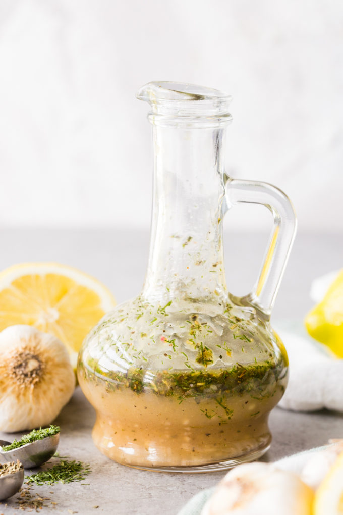 Bottle of Greek Chicken Marinade with lemons, garlic, and herbs around it. 