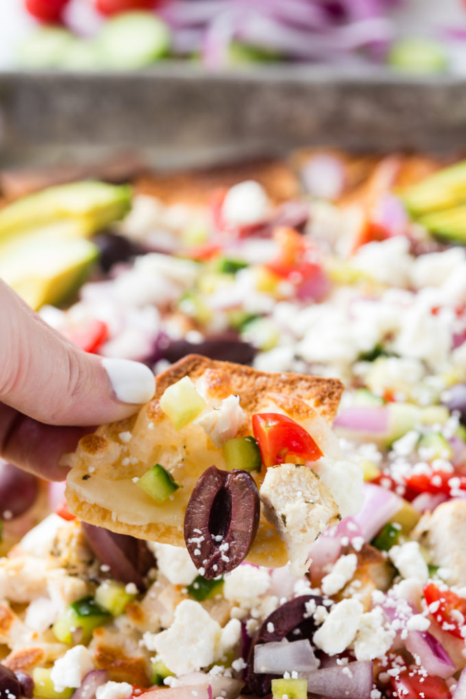 greek chicken nachos with a hand using a pita chip to scoop.