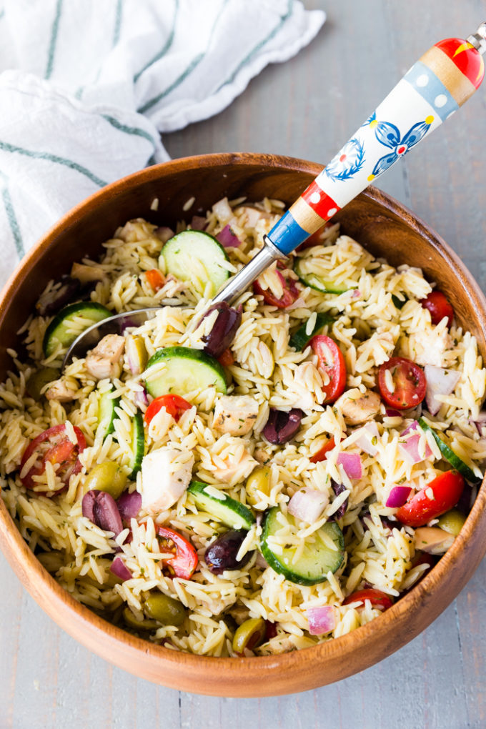 Brown bowl with greek chicken orzo pasta salad inside and spoon.