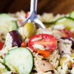 greek chicken orzo pasta salad in a brown bowl with a silver spoon.