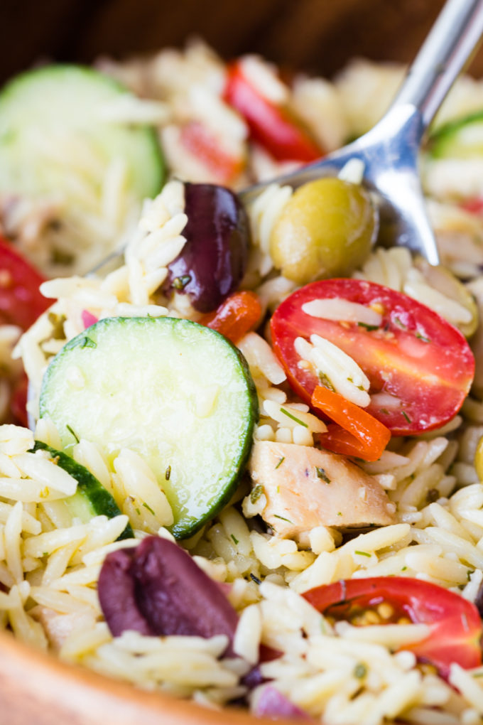greek chicken orzo pasta salad in a bowl with spoon. Close up.