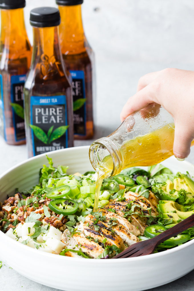 A white bowl full of grilled chicken salad and a hand pouring a dressing over top. 