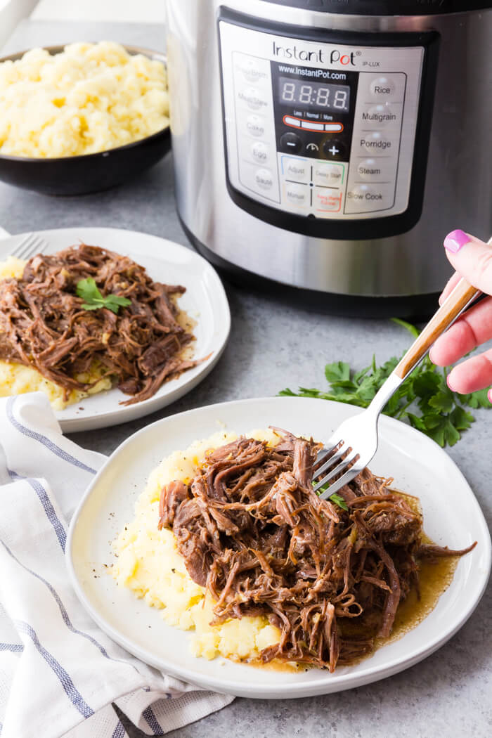 Pressure cooker pot roast on a bed of mashed potatoes in front of an instant pot