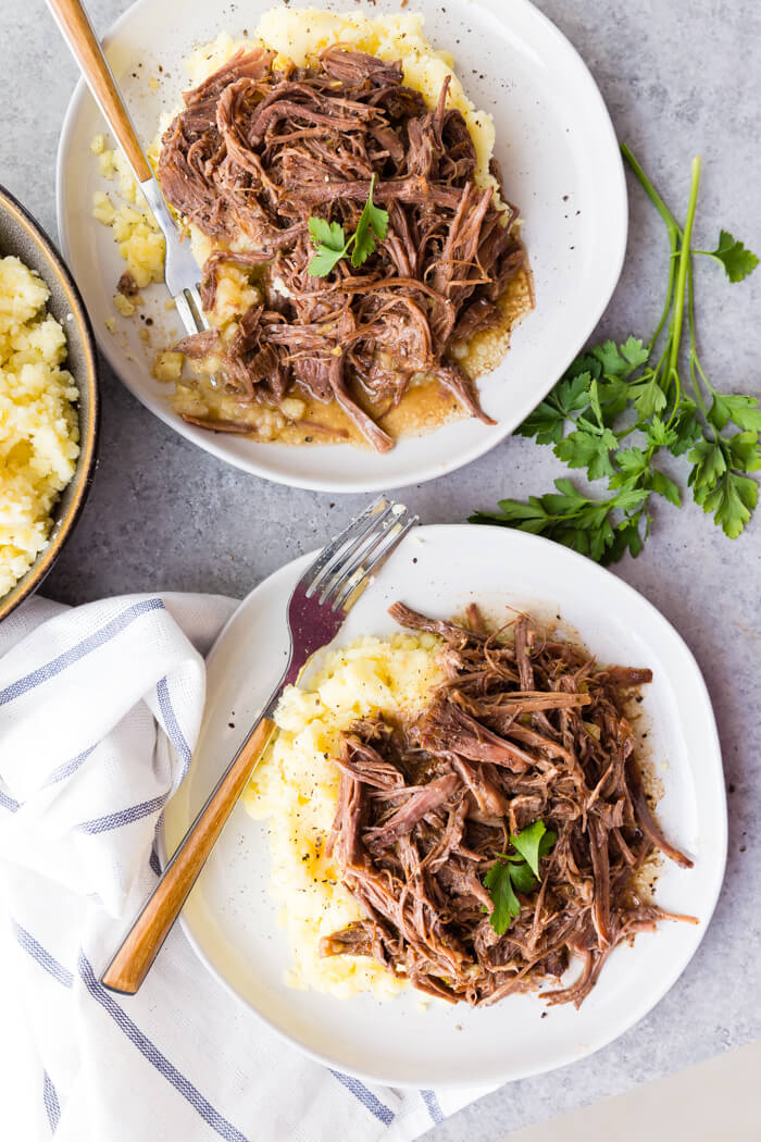 instant pot Mississippi pot roast with creamy mashed potatoes topped with black pepper and parsley on a white plate with a fork