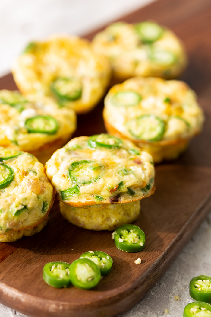 six jalapeno popper egg muffins on a cutting board with some sliced jalapenos