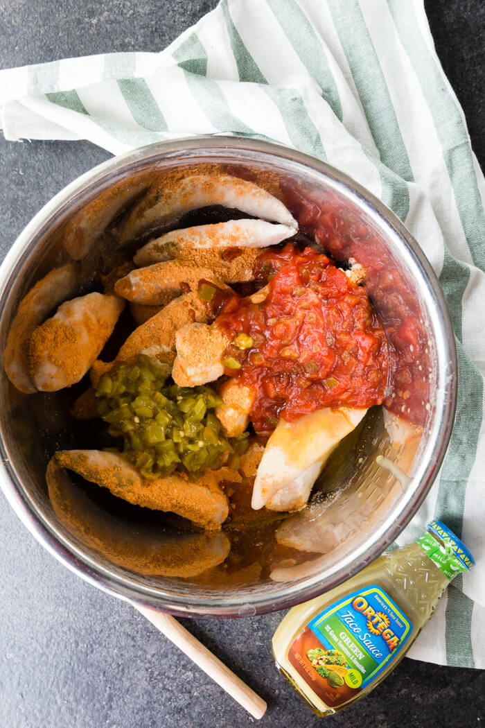 salsa and seasonings on top of frozen chicken in a metal bowl