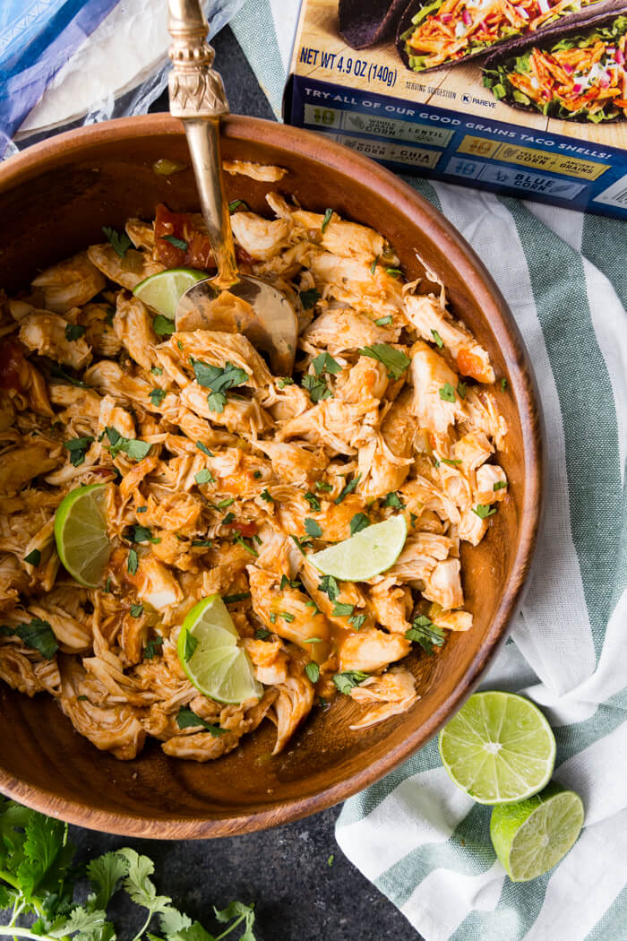 Shredded Chicken made in a pressure cooker served in a wooden bowl with a metal spoon with limes and parsley as garnish