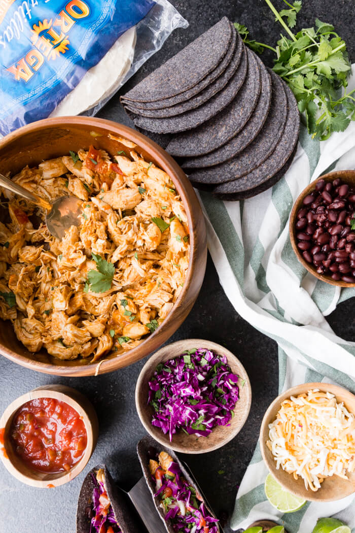 Instant Pot Shredded Chicken, Salsa, Cabbage, Cheese, and Black Beans in wooden bowl ready for a taco bar with blue corn taco shells 