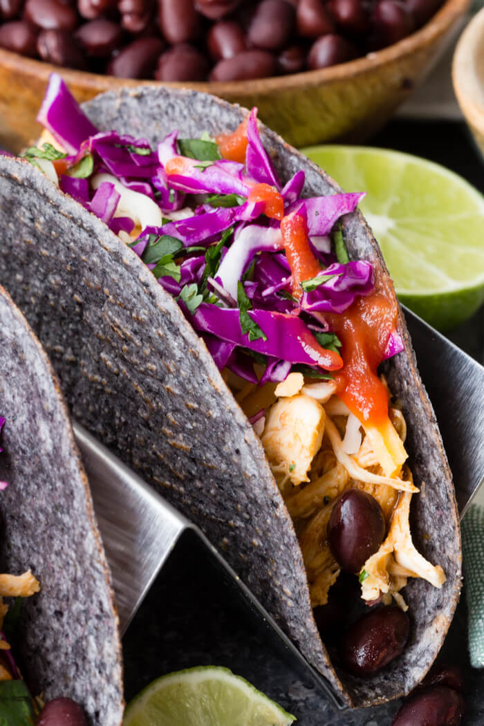 a blue corn taco shell filled with slow cooker Mexican shredded chicken, black beans, and veggies in a metal taco holder 