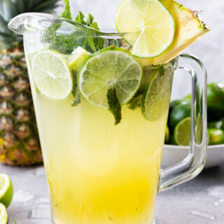 Pineapple Mojito in a pitcher with limes, mint, and pineapple juice