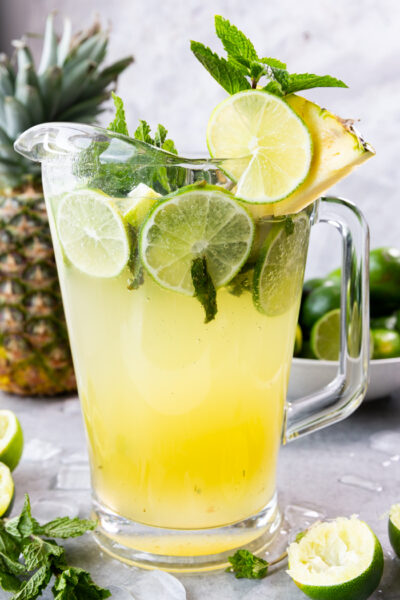 Pineapple Mojito in a pitcher with limes, mint, and pineapple juice