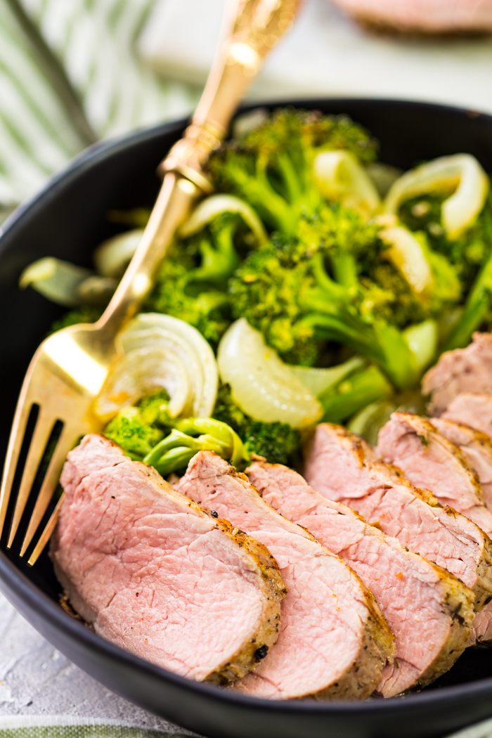 Pork tenderloin on a black bowl with vegetables and sliced pork tenderloin