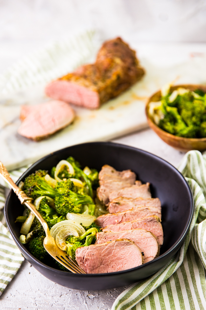 Pork tenderloin with roasted vegetables. In a black bowl, with a tenderloin in the background