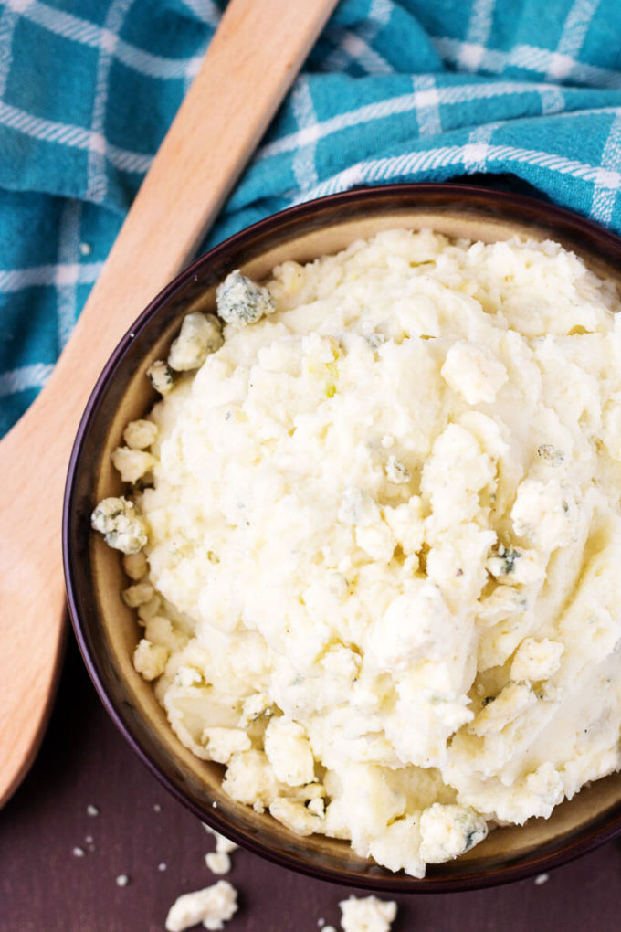 Top down view of Roasted Garlic Bleu Cheese Mashed Potatoes in a bowl with a wooden spoon.