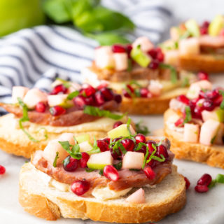 Roasted Pork Crostini with apple and pomegranate on a marble cutting board