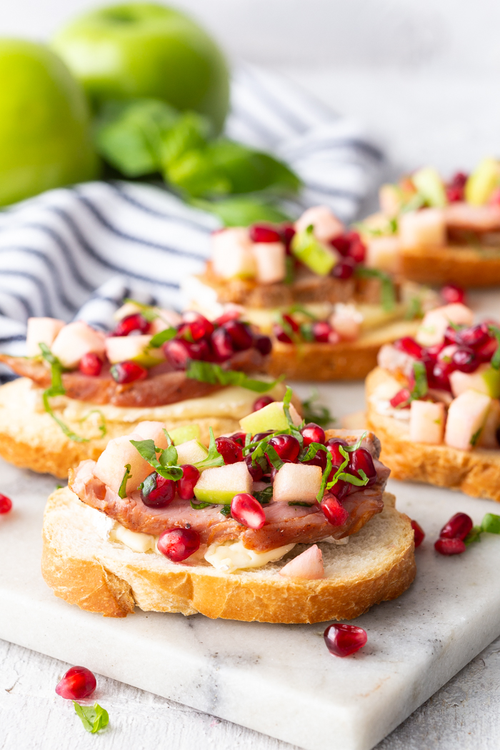 Roasted Pork Crostini with apple and pomegranate on a marble cutting board