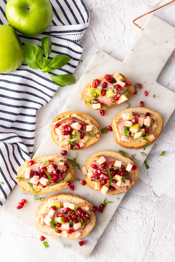 A great holiday appetizer, a crostini topped with brie, roasted pork tenderloin, apples and pomegranate