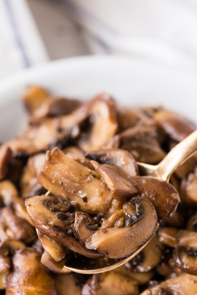Sautéed mushrooms in a white serving dish with a gold spoon